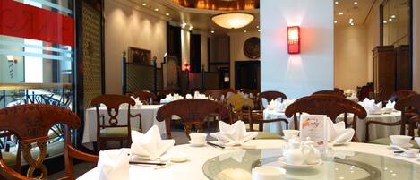 A restaurant with round tables set for dining, wooden chairs, and a glass-top table centerpiece.