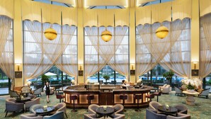 Un hall de hotel con zona de bar, espacios de descanso y grandes ventanales.