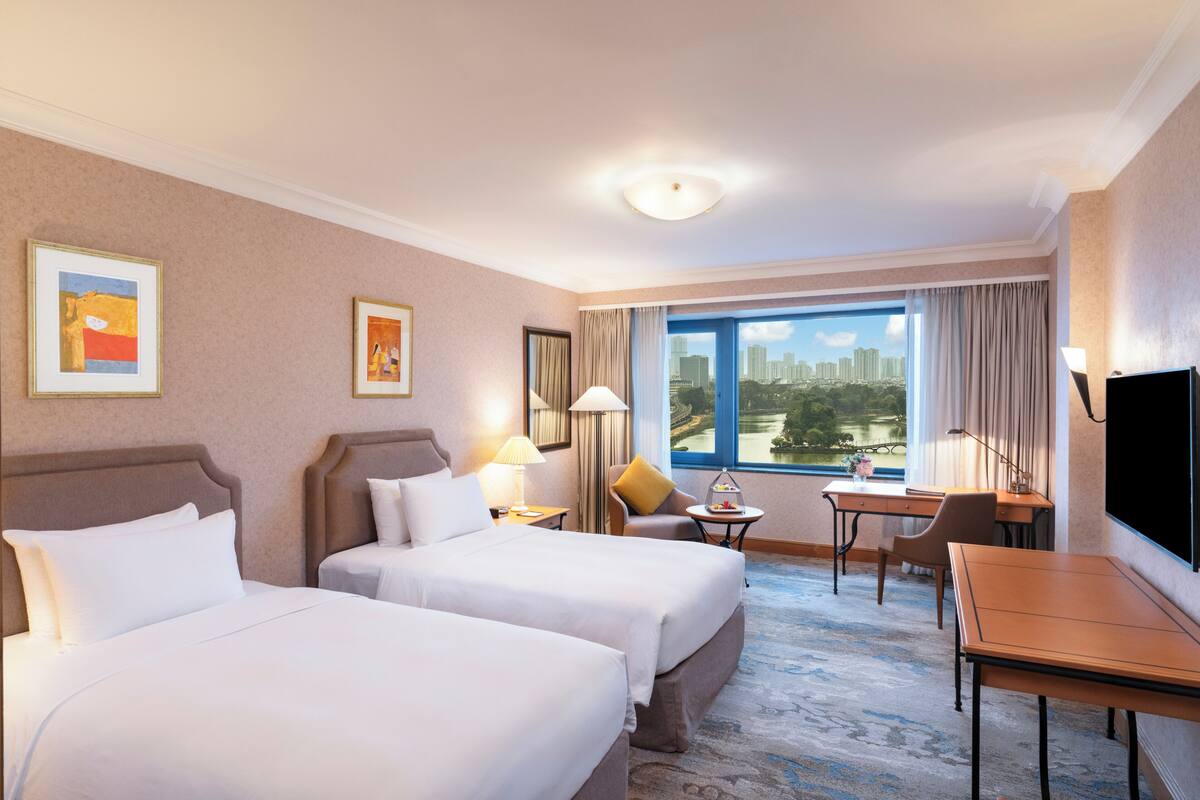 A hotel room with two beds, a desk, a chair, a TV, and a window with a city view.