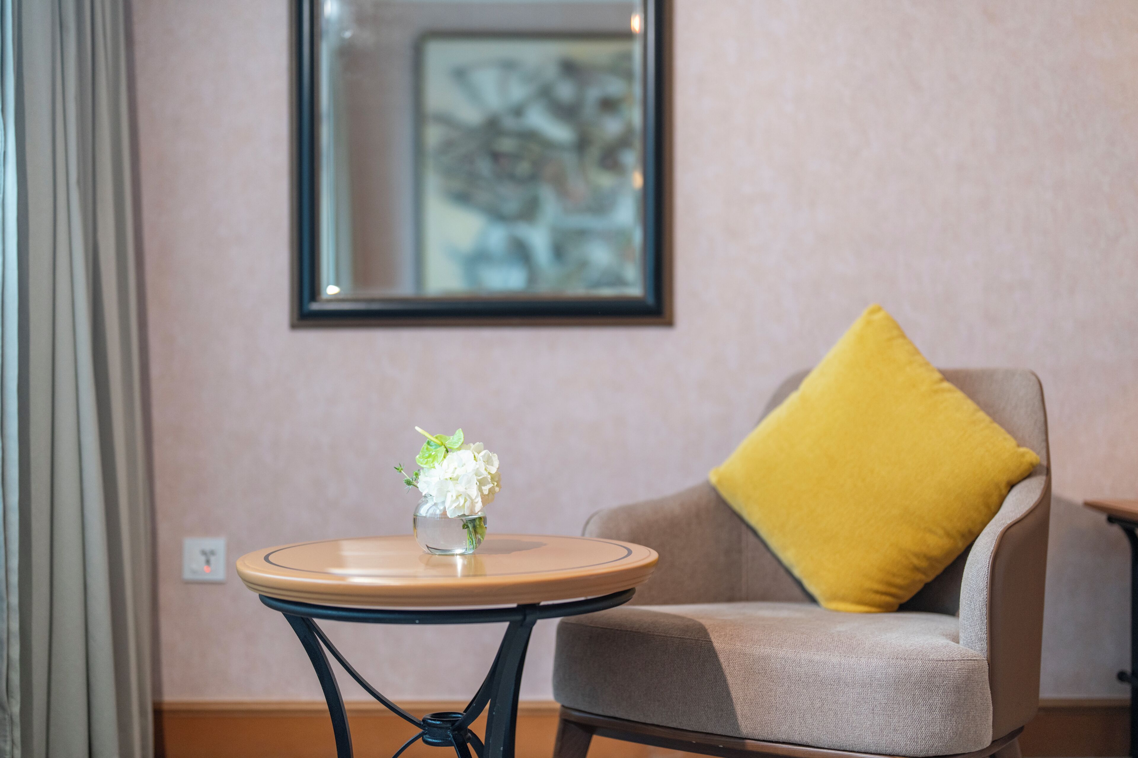 Una habitación con una mesa redonda, una silla con un cojín amarillo y una obra de arte enmarcada en la pared.