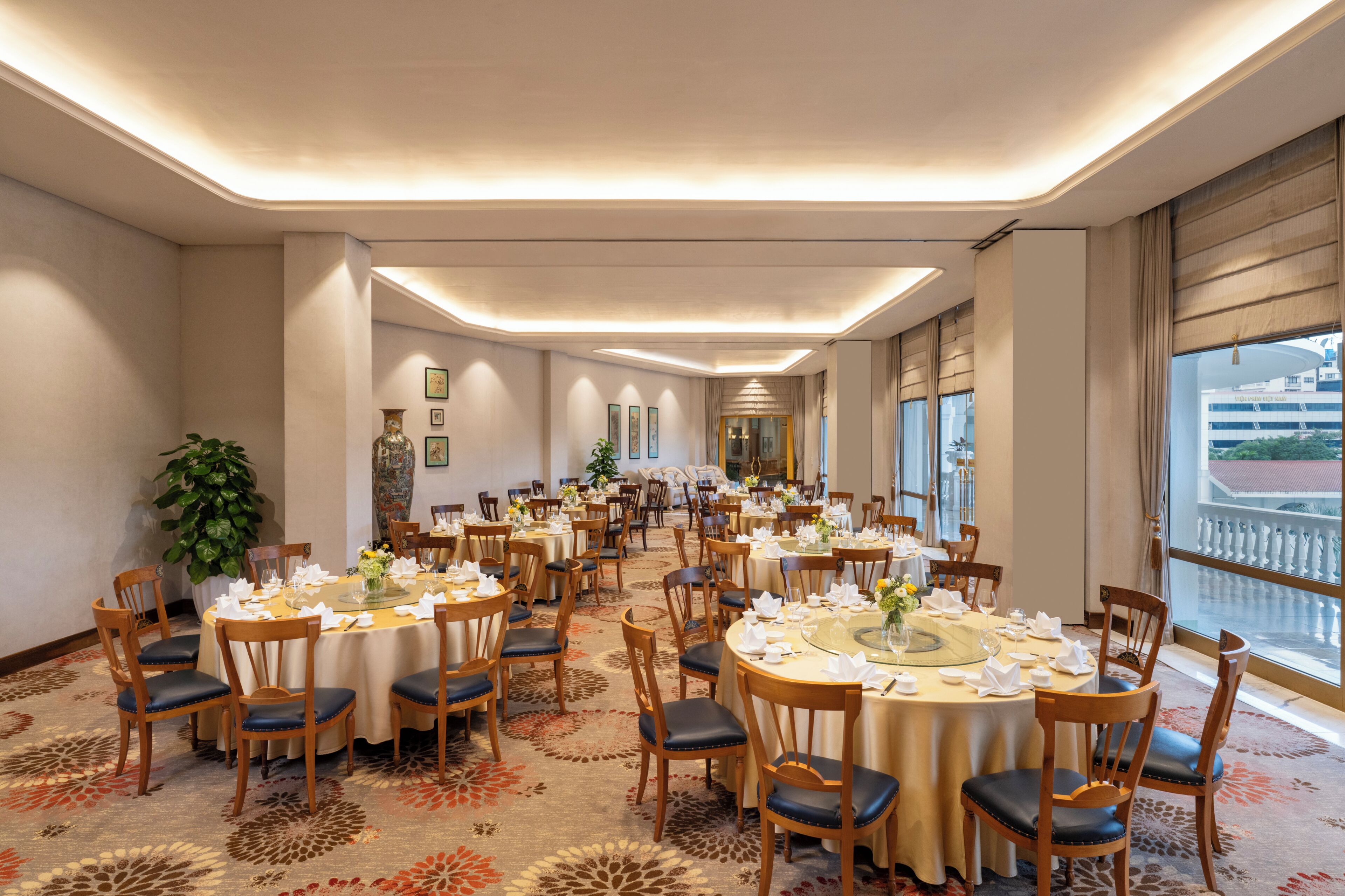 Une grande salle de banquet avec des tables rondes, des chaises et un sol recouvert de moquette.
