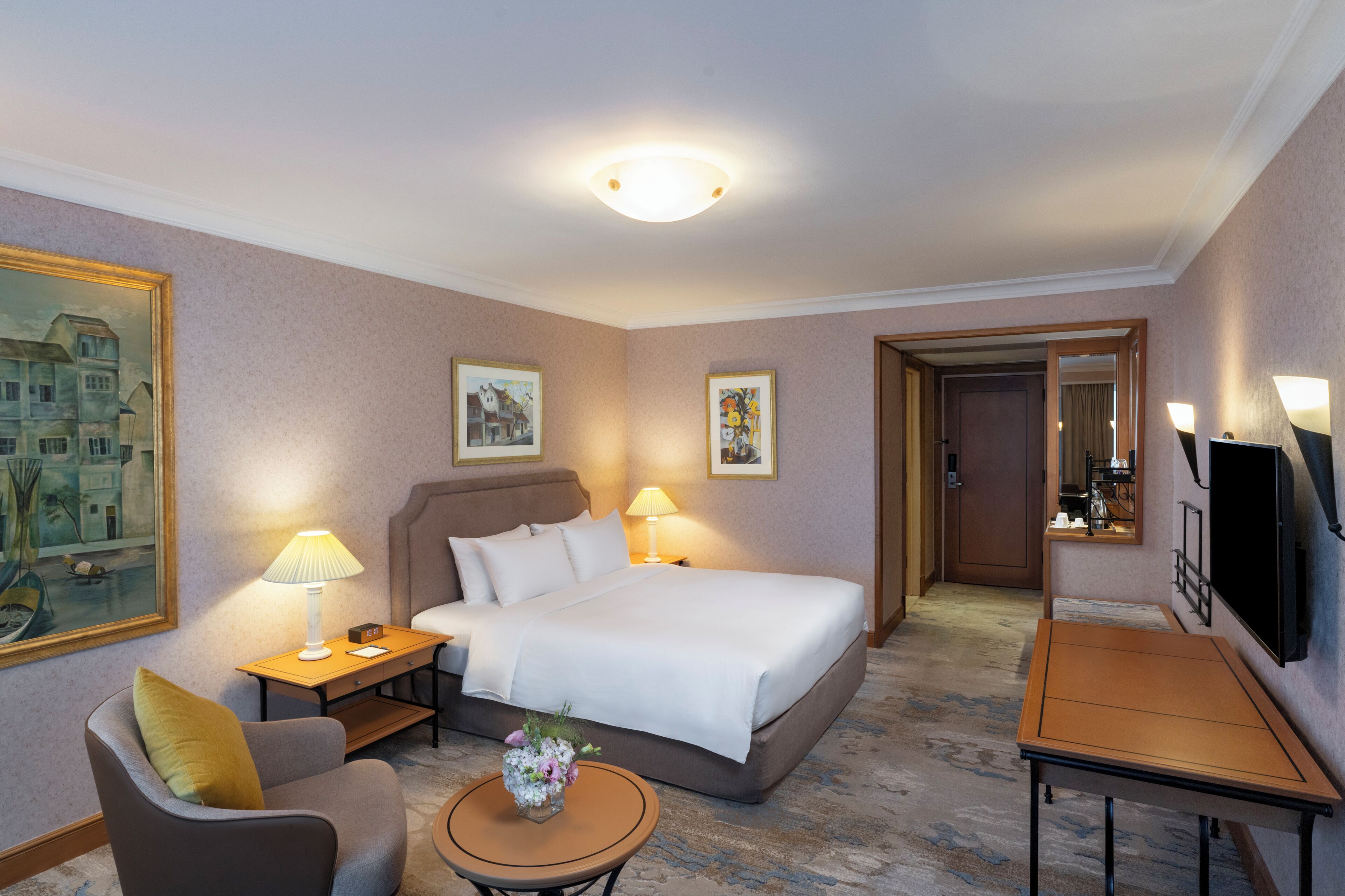 A hotel room with a bed, bedside tables, a chair, a small table with a vase, and a TV.