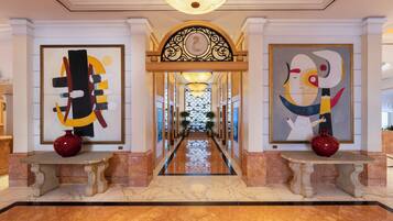 A hallway with marble flooring, two large abstract paintings, a decorative archway, and a chandelier.