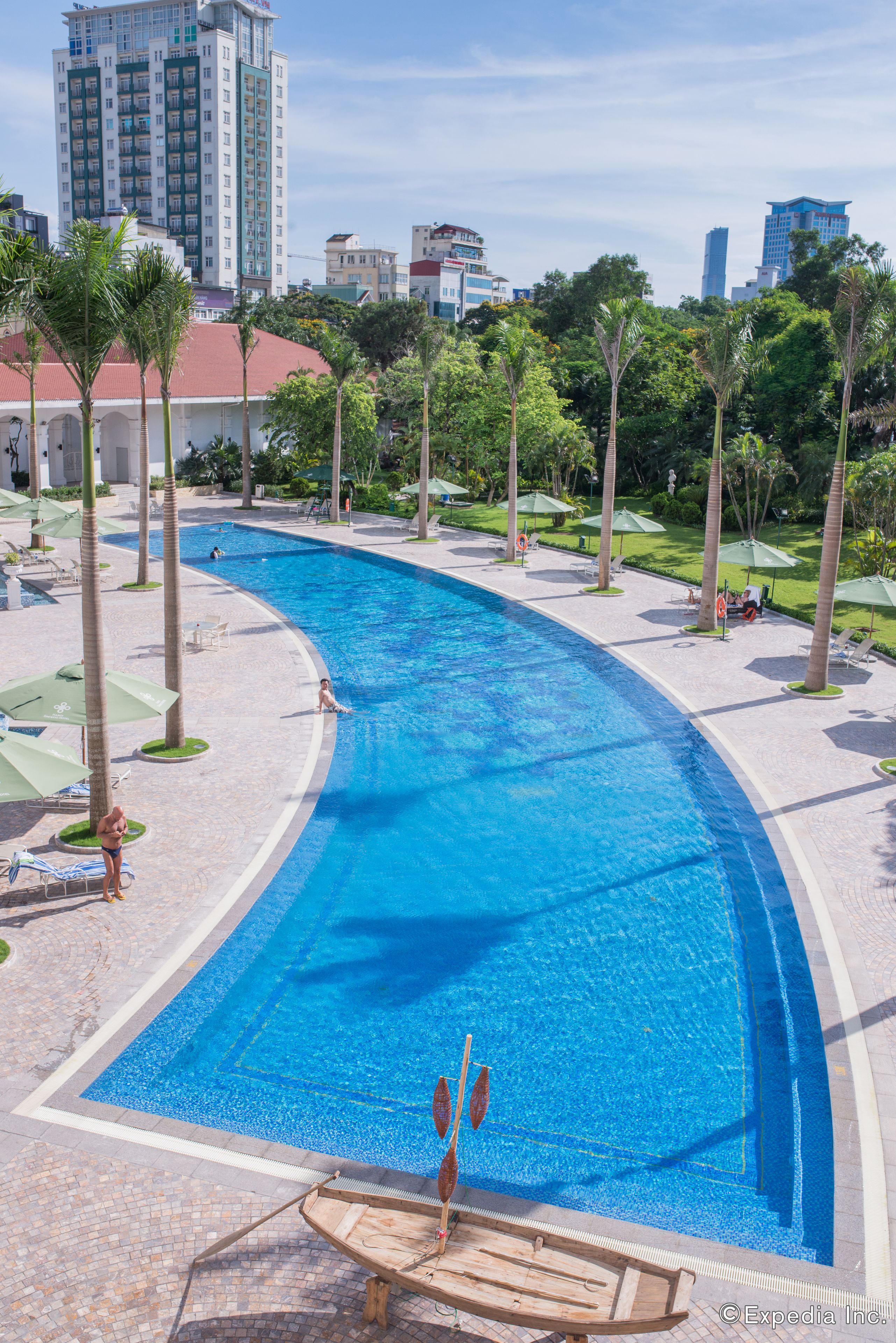A large swimming pool with a curved edge, surrounded by palm trees and lounge chairs.