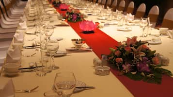 A long banquet table set with white tableware, red tablecloth, and floral centerpieces.