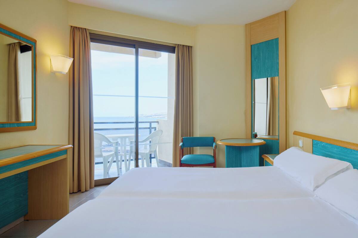 Habitación de hotel con cama, escritorio, silla, una mesita y balcón con vistas.