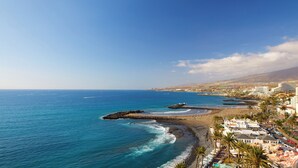 A coastal town with a beach, rocky shoreline, and buildings along the shore. - Sol Tenerife (Arona)