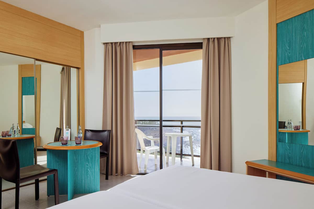 Habitación de hotel con una cama grande, un escritorio con silla, una mesita y un balcón con vistas.