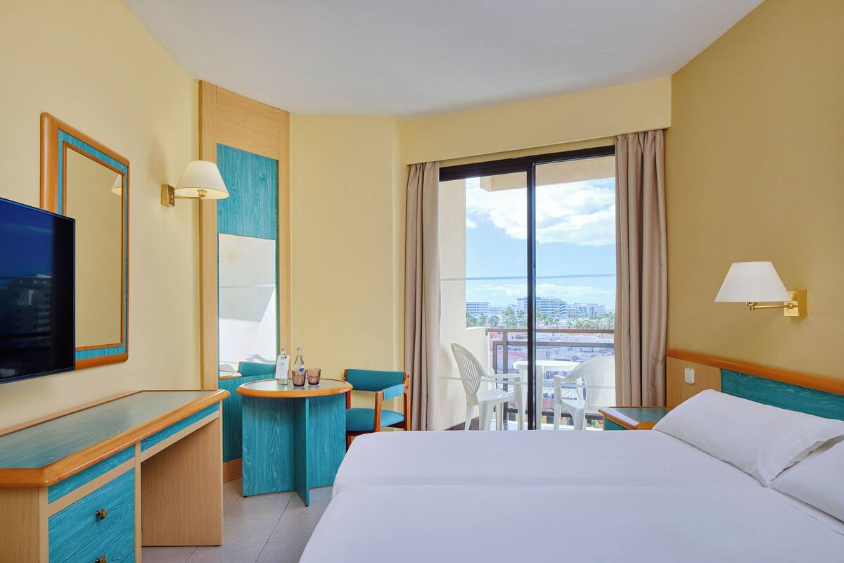 Habitación de hotel con cama, escritorio, silla, una mesita con bebidas y balcón con vistas.