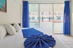 A hotel room with a bed, pillows, a blue blanket, and a view of a building through a glass door.