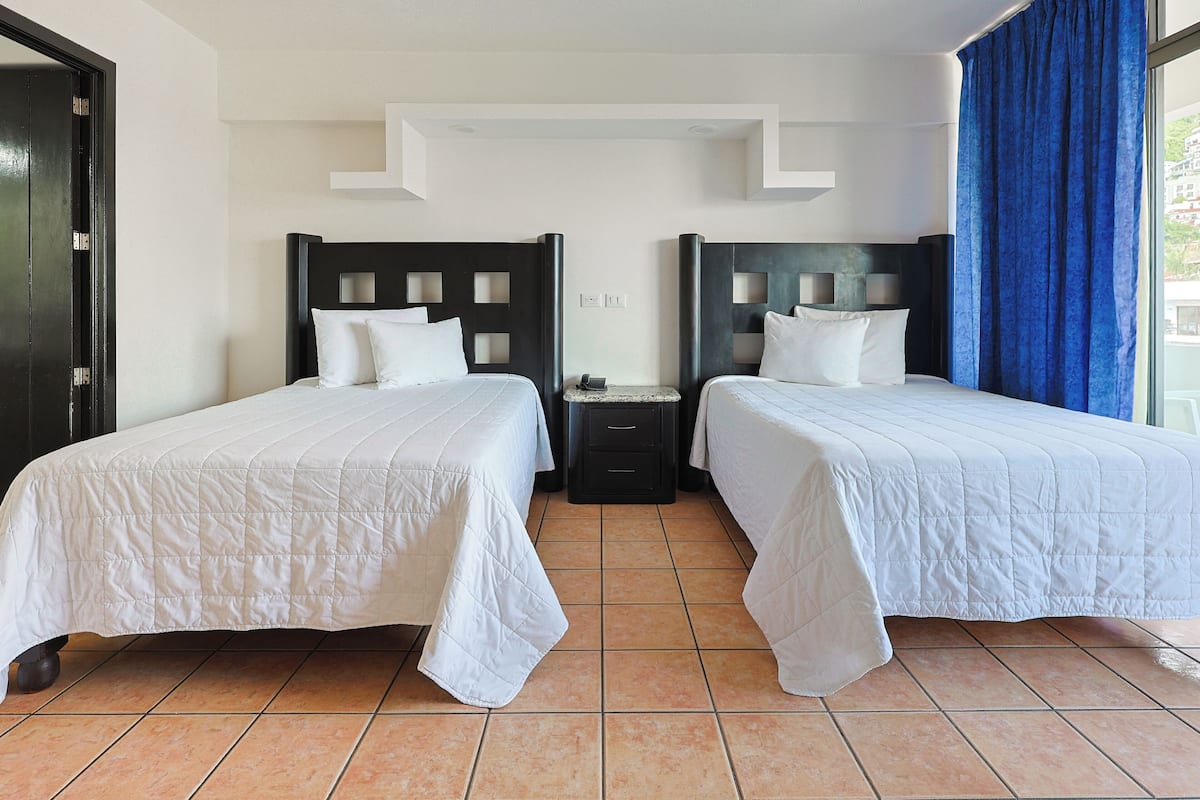 A hotel room with two beds, a nightstand, and a window with blue curtains.