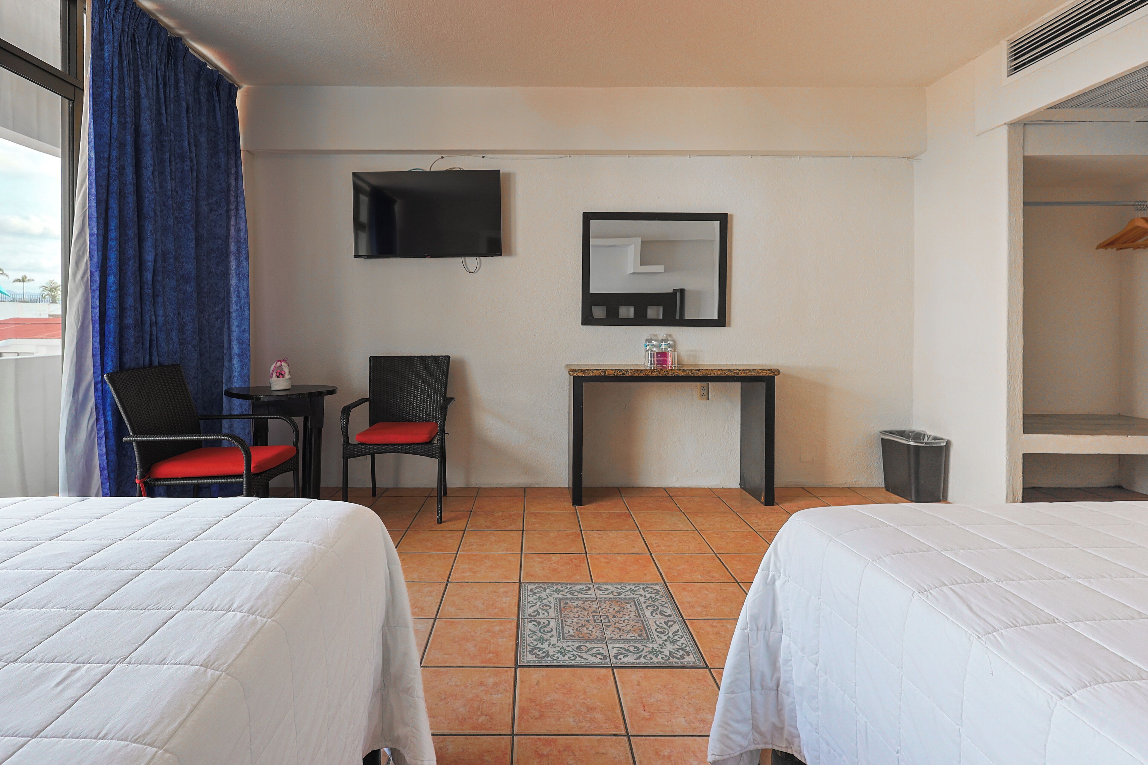 Une chambre d’hôtel avec deux lits, un bureau, une chaise, une télévision et un miroir.