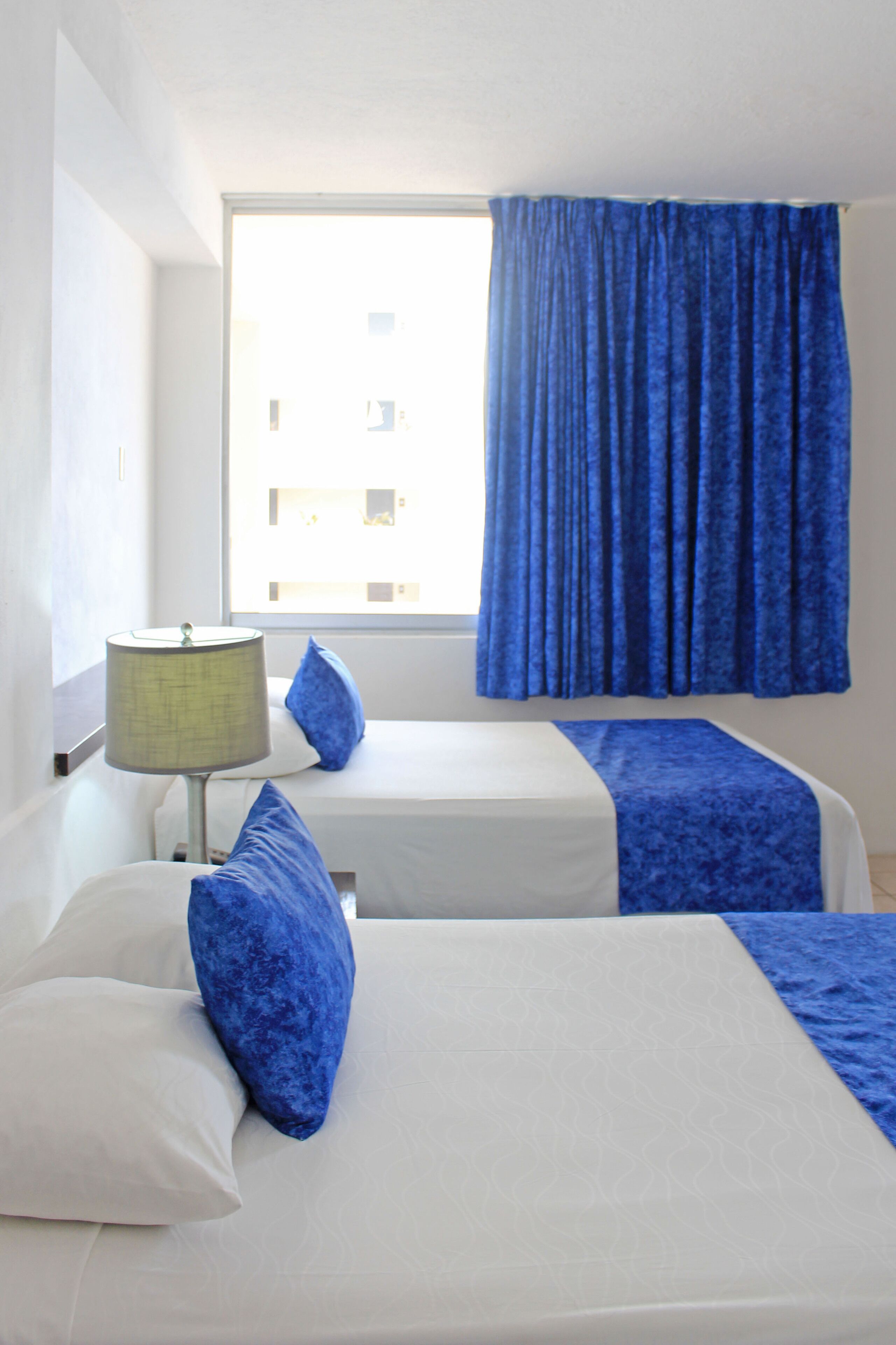 Een hotelkamer met twee bedden, een raam met gordijnen en een lamp.