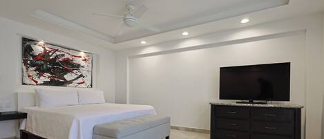 A bedroom with a bed, a TV, a ceiling fan, and artwork on the wall.