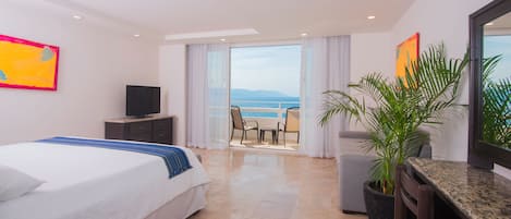 Een hotelkamer met een bed, een televisie, een balkon met uitzicht op zee en een potplant.