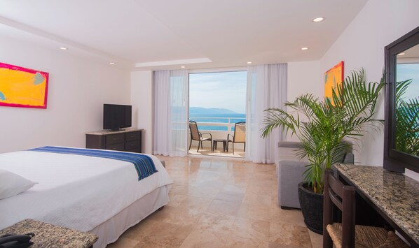 A hotel room with a bed, a TV, a balcony with a view of the sea, and a potted plant.