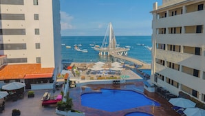 A hotel with a pool, outdoor seating, and a view of the sea and a bridge.