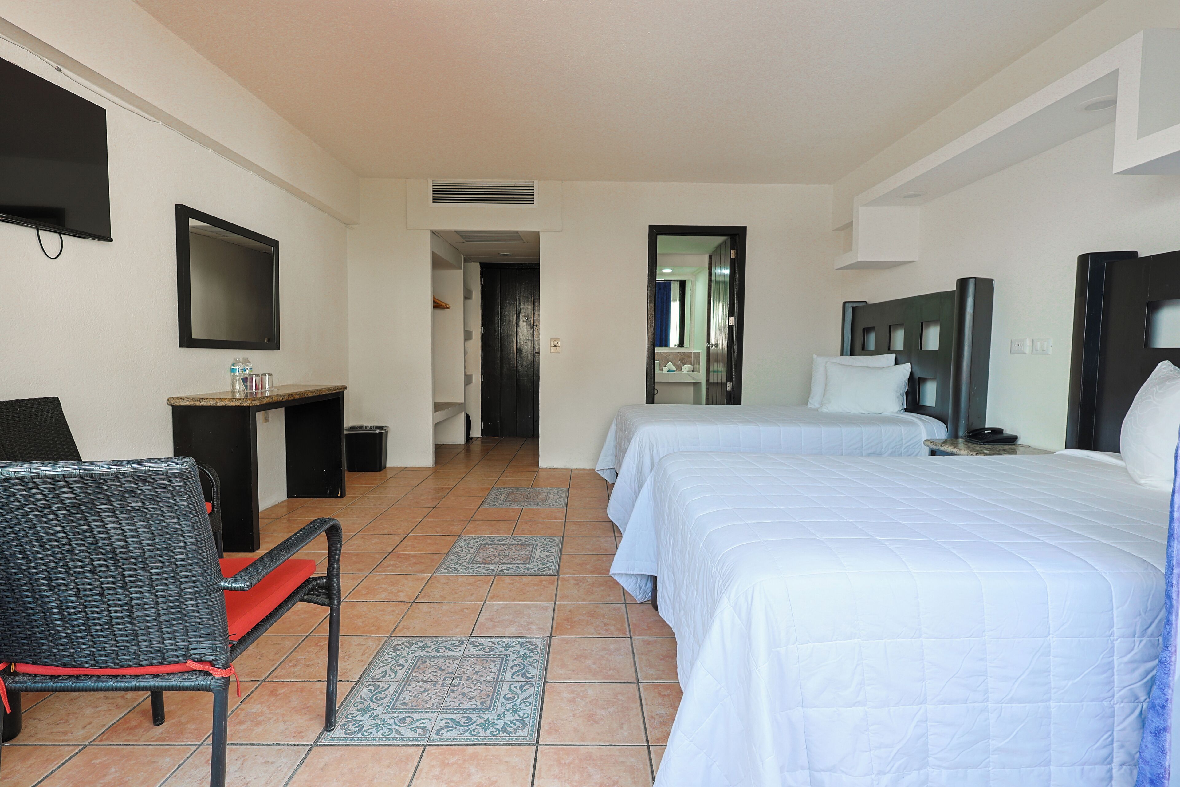 A hotel room with two beds, a TV, a desk, and a chair.