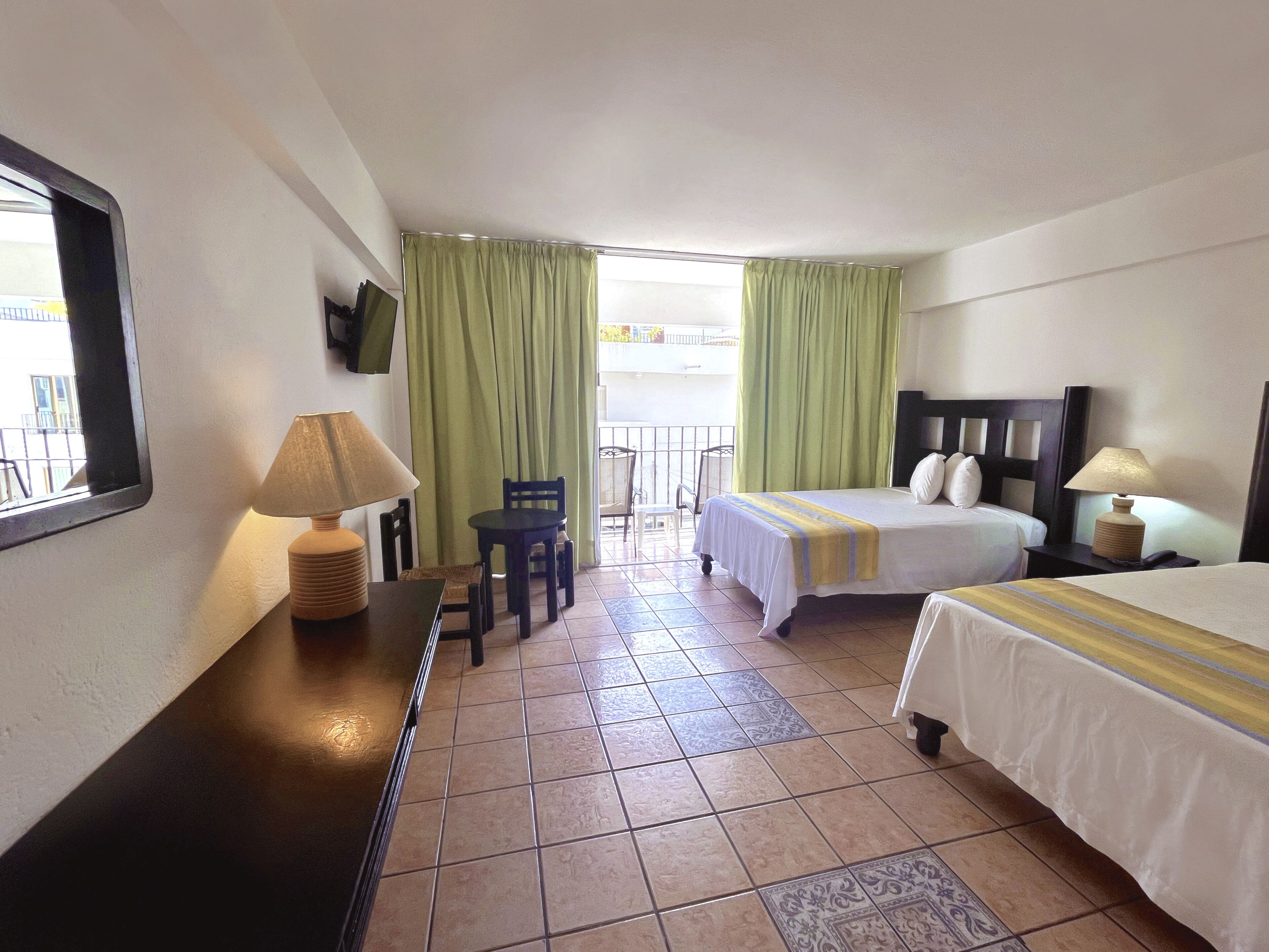 A hotel room with a bed, a desk with a lamp, a chair, and a TV on the wall.