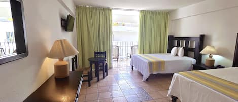 A hotel room with a bed, a desk with a lamp, a chair, and a TV on the wall.