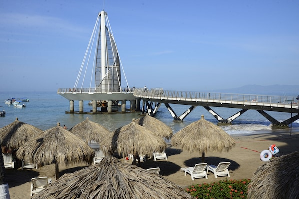 Une plage avec des parasols en chaume, des chaises longues et une jetée où est amarré un bateau.