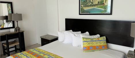 A hotel room with a bed, a nightstand, a lamp, a small table, and a framed picture on the wall.
