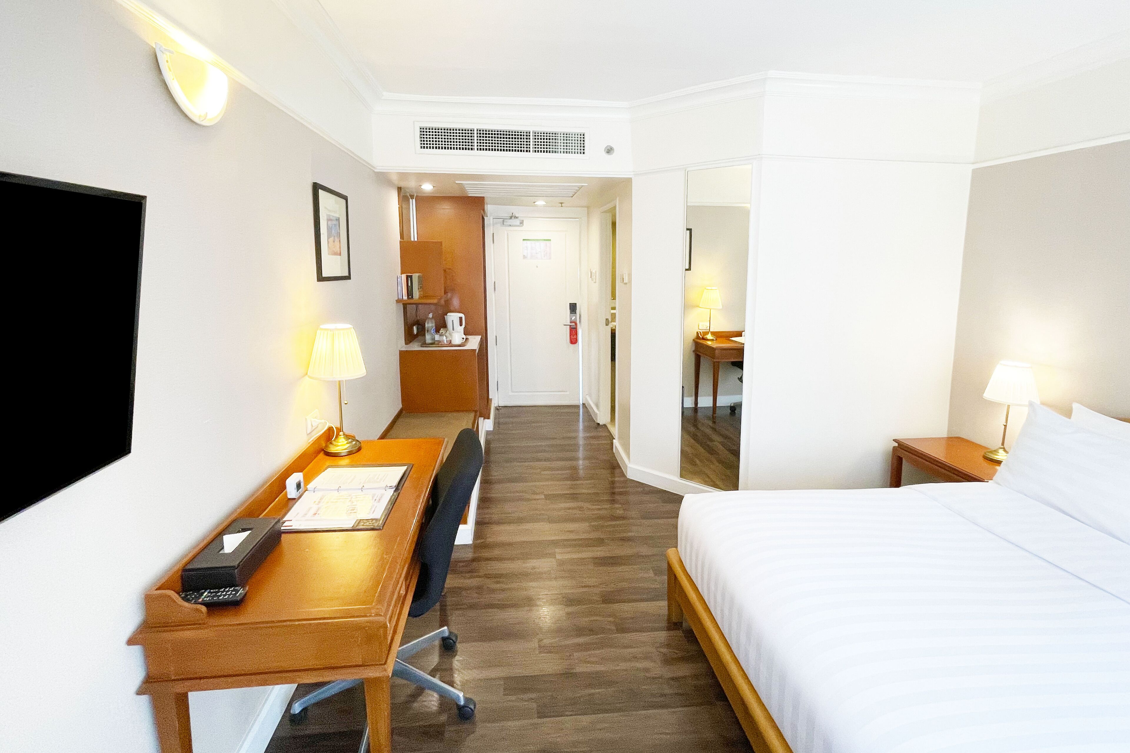 A hotel room with a bed, desk, chair, and a television.