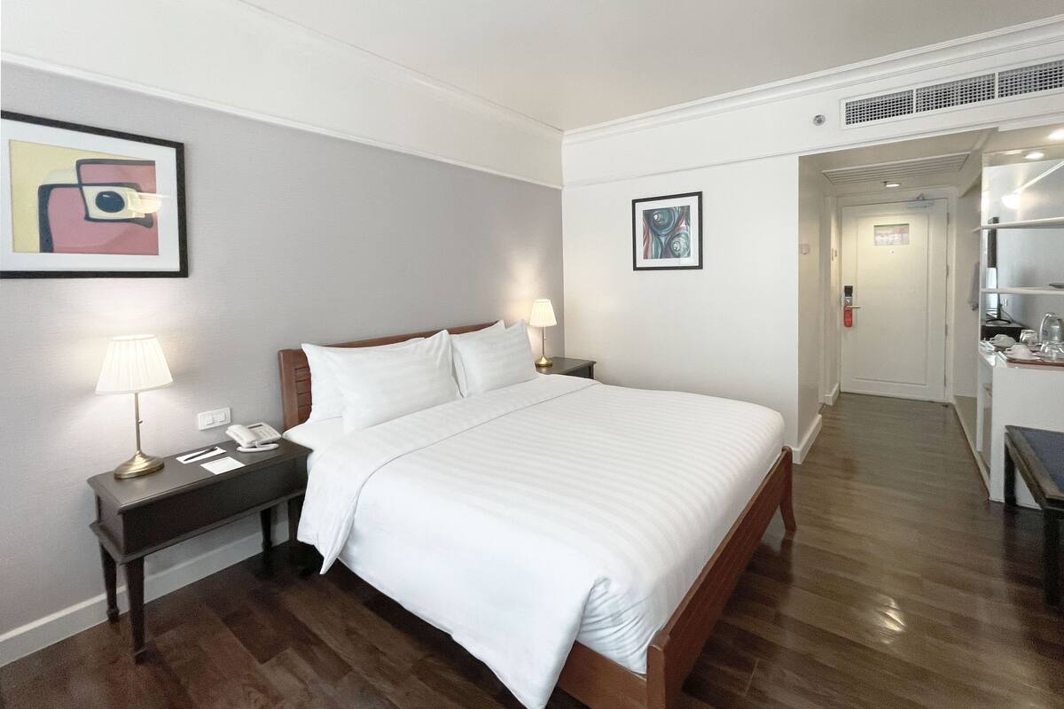 A hotel room with a large bed, a nightstand with a lamp, and a desk with a chair.