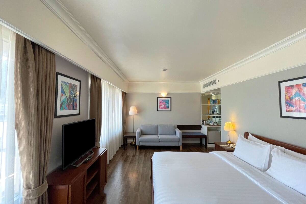 A hotel room with a bed, a television, a sofa, a desk, and a bookshelf.