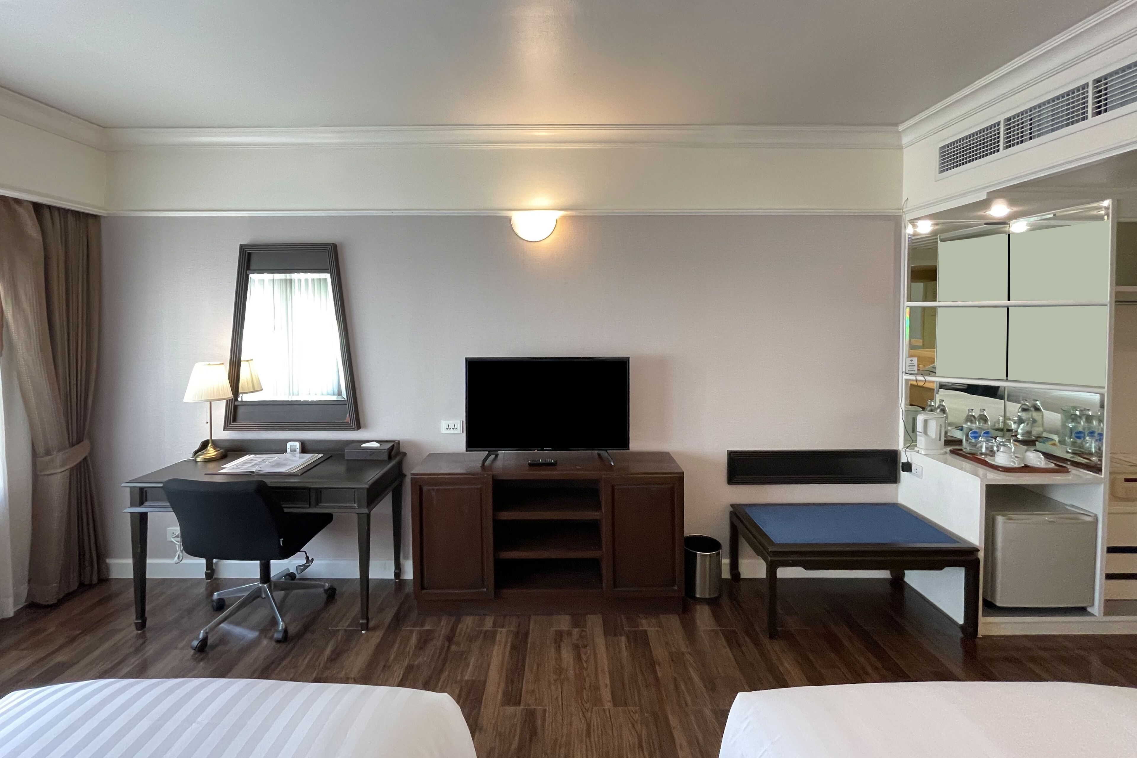 A hotel room with a bed, a desk with a chair, a television, a small table, and a mirror.