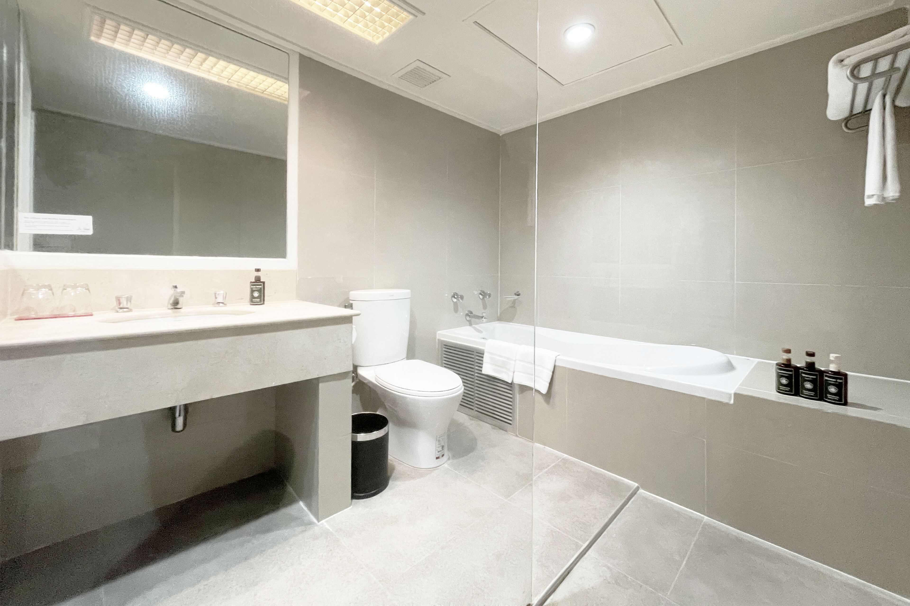 A modern bathroom with a large mirror, a toilet, a sink, and a bathtub.