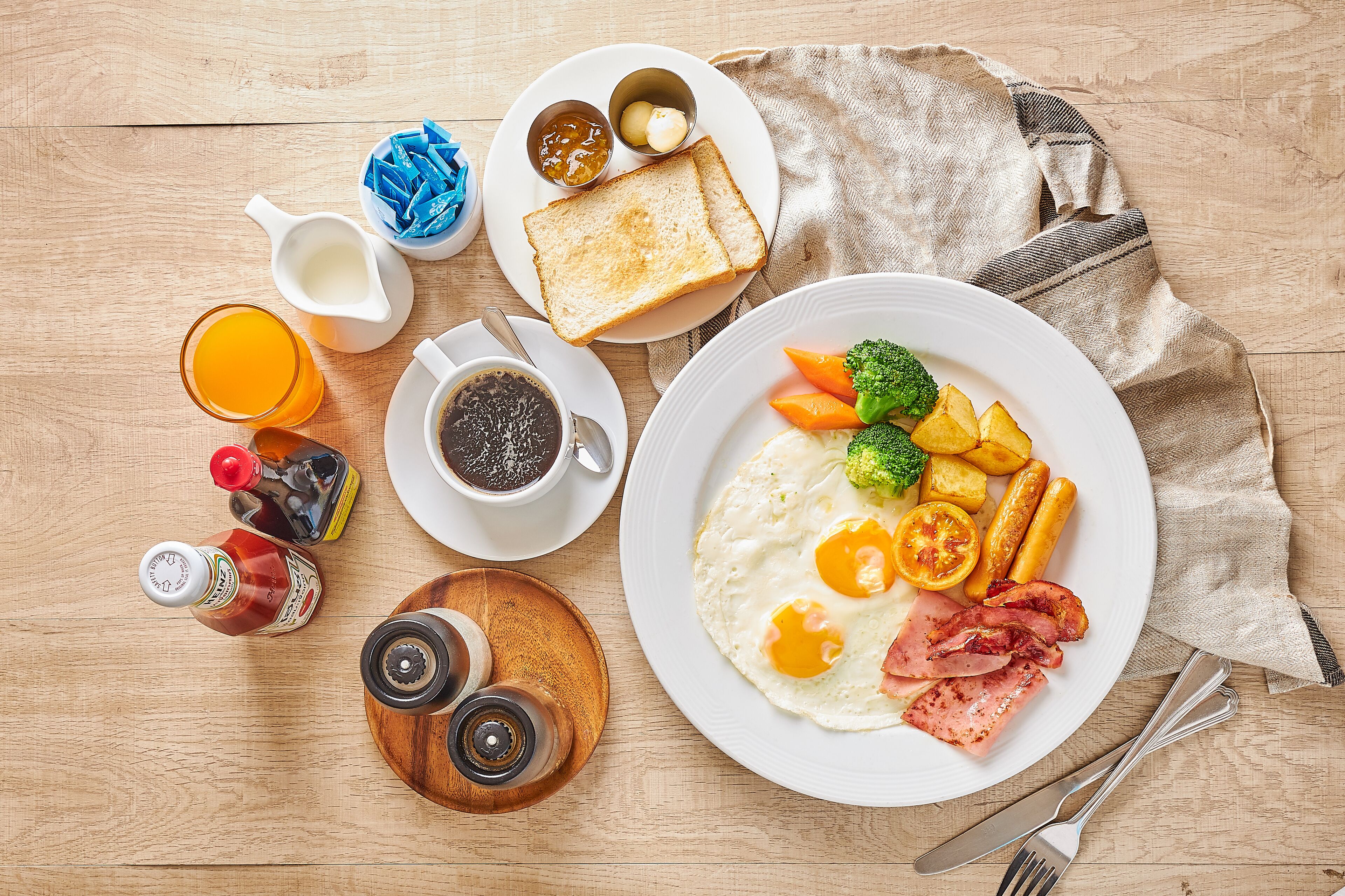 A breakfast plate with eggs, bacon, and vegetables, a cup of coffee, and condiments on a wooden table.
