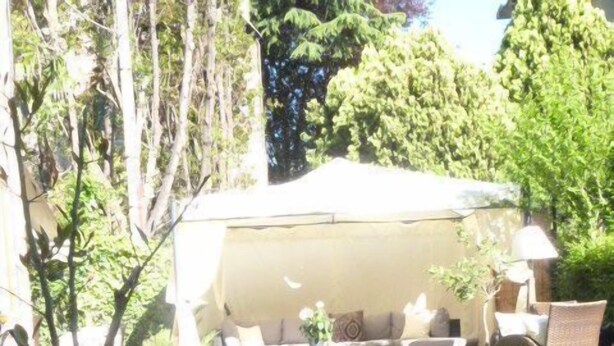 A covered outdoor seating area with a sofa and chairs, surrounded by lush greenery and flowering plants. - Hotel Villa Stella.check-in.9AM-3PM (Venice)