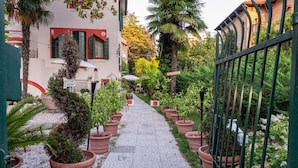 A narrow pathway lined with potted plants leading to a building with a red awning and a sign that reads "BISTROT". - Hotel Villa Stella.check-in.9AM-3PM (Venice)