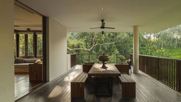 A wooden deck with a dining table and benches, a ceiling fan, and a view of lush greenery.