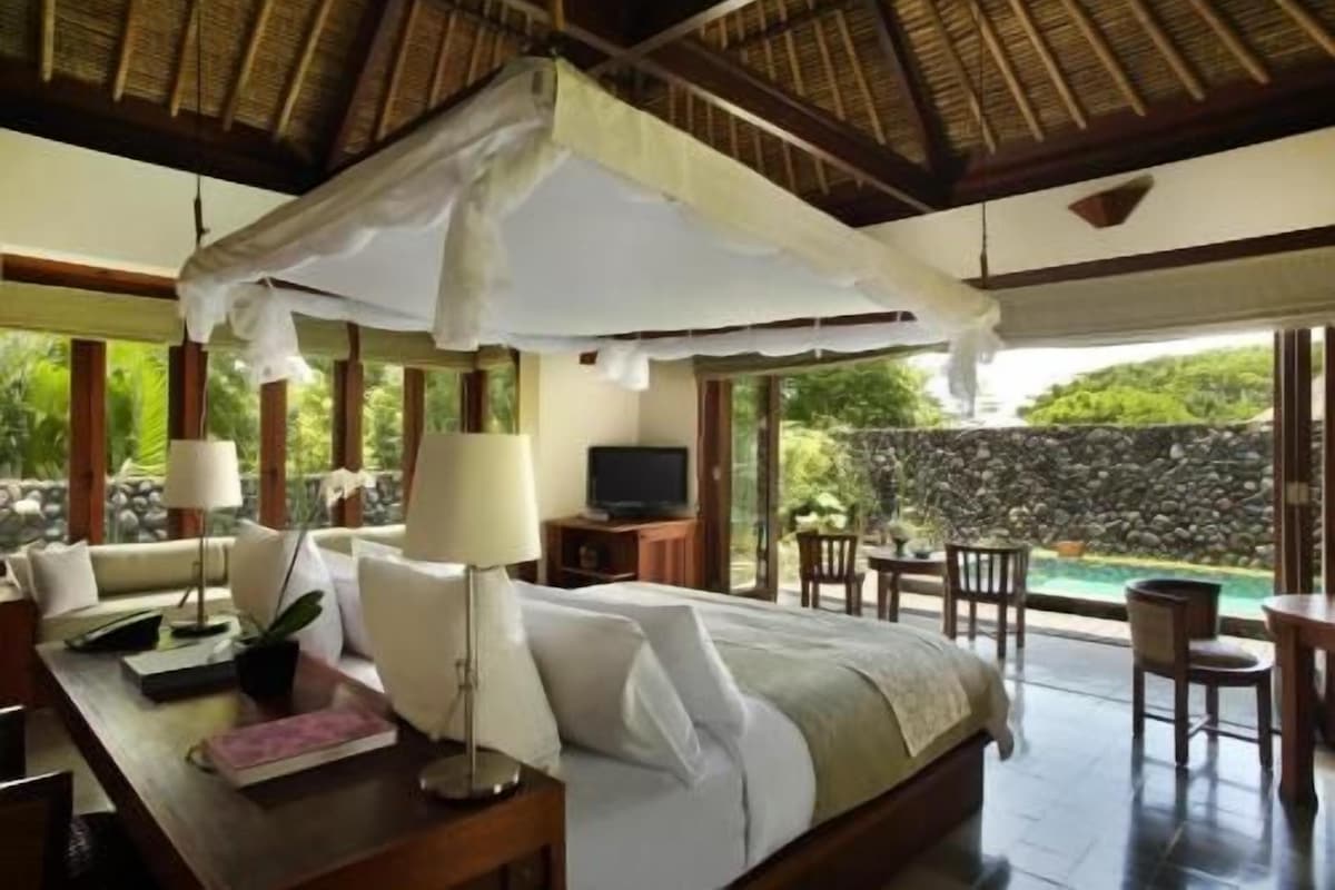 Un dormitorio con cama, mesita de noche, lámpara y vista a una piscina.