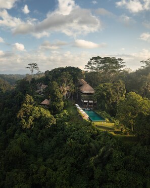 A resort with multiple buildings surrounded by dense forest, a swimming pool, and a clear sky. - Alila Ubud. Bali (Ubud)