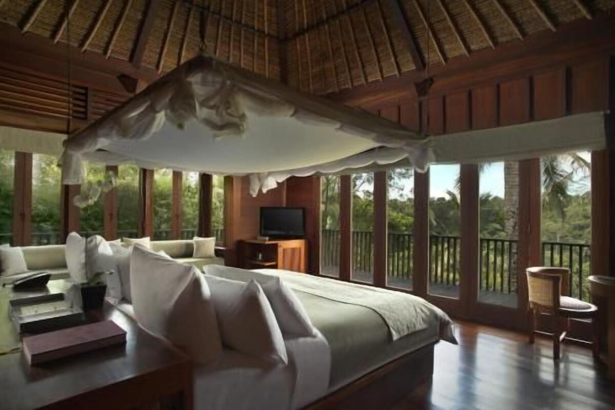 Un dormitorio con cama con dosel, televisor y balcón con vistas al verdor.