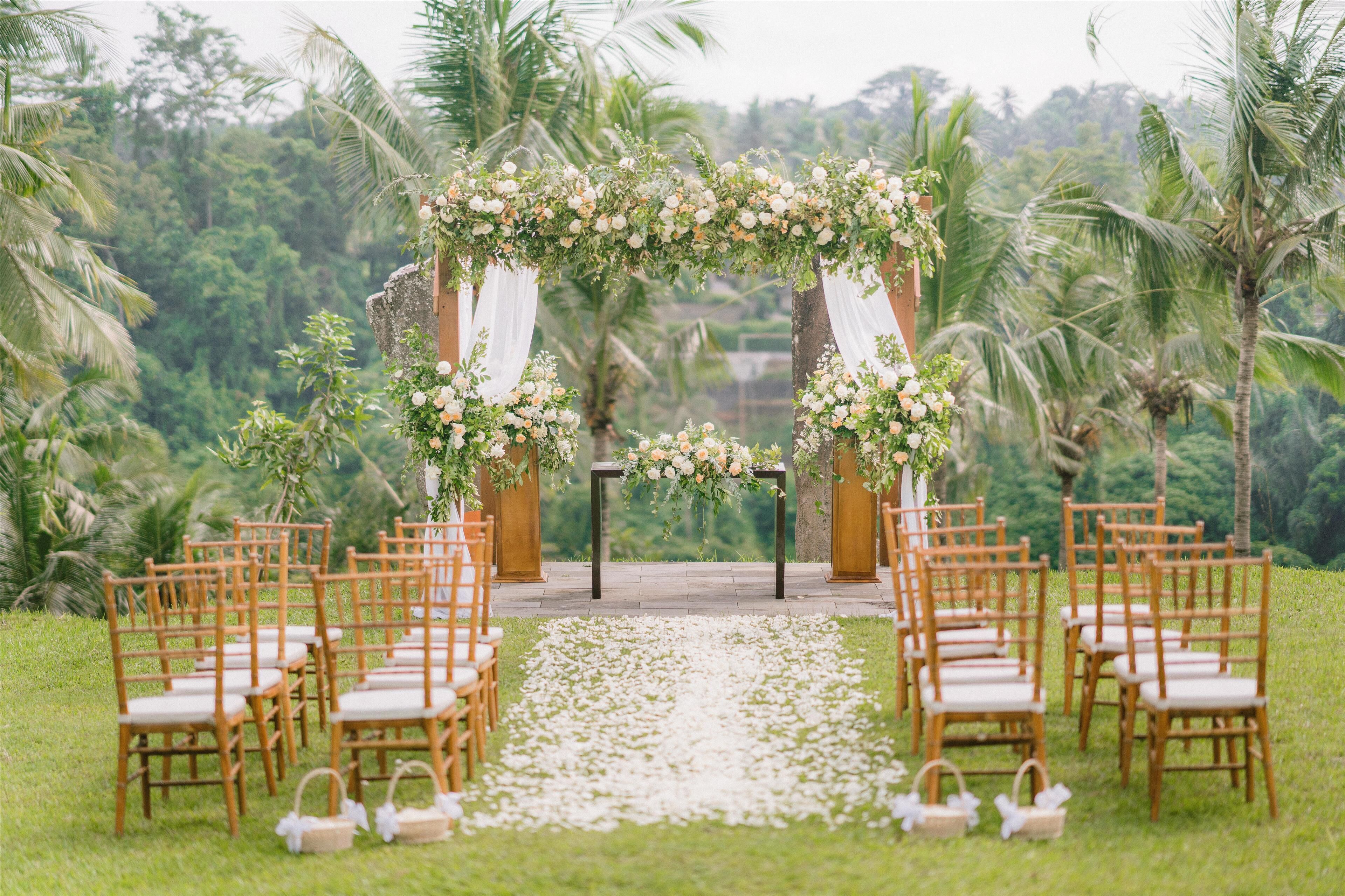 A wedding ceremony setup with a floral arch, wooden chairs, and a white aisle.