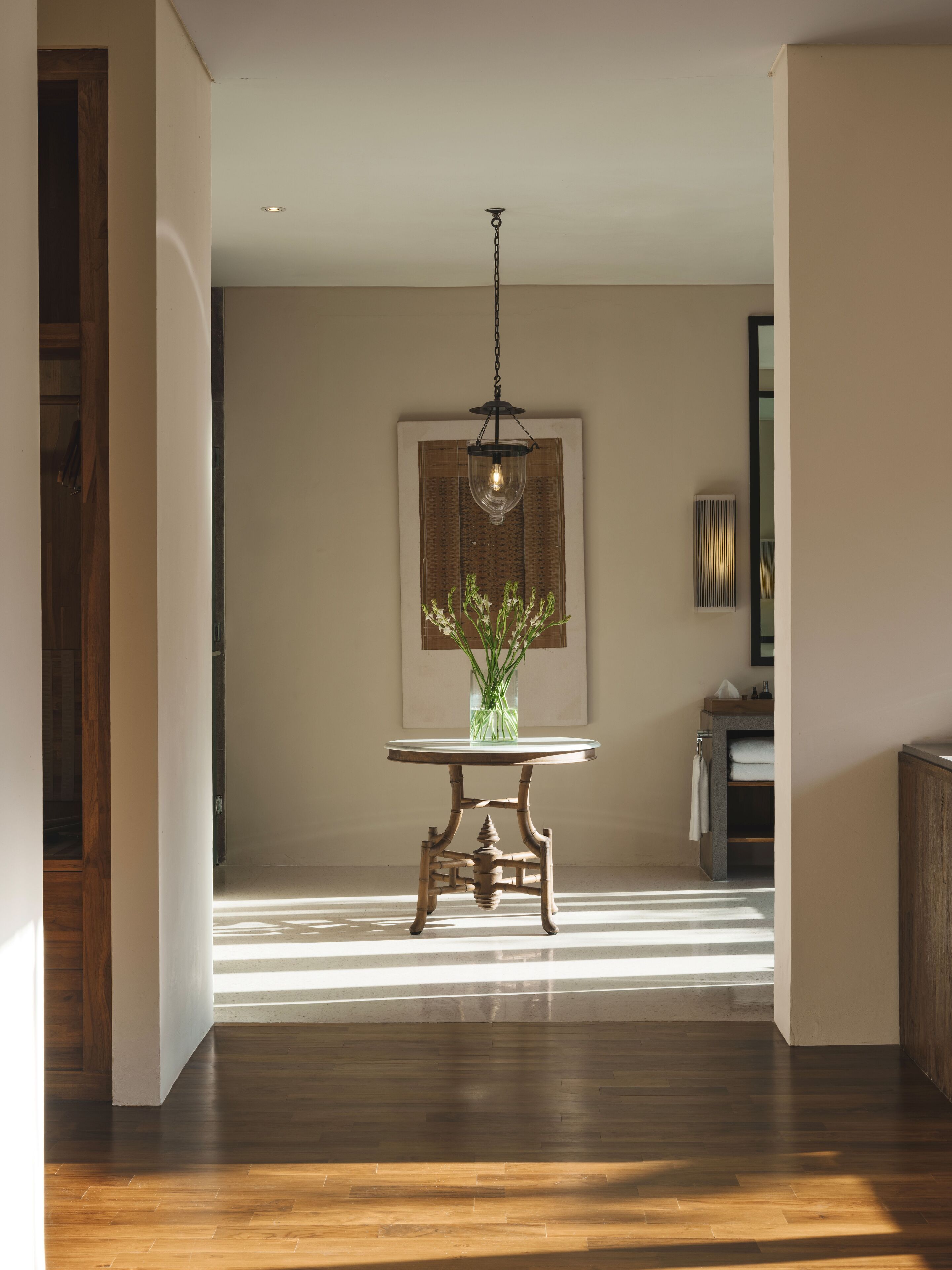 A modern interior with a wooden floor, a round table with a vase of green plants, and a hanging light fixture.