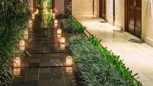 A pathway lined with lanterns leading to a building with wooden doors and a stone wall.