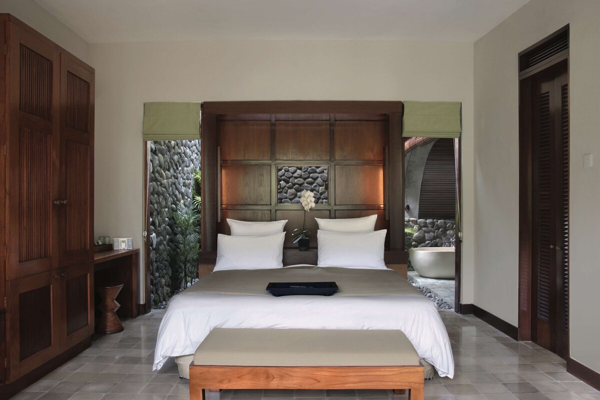 A large bed with a headboard, a bedside table, and a bench.