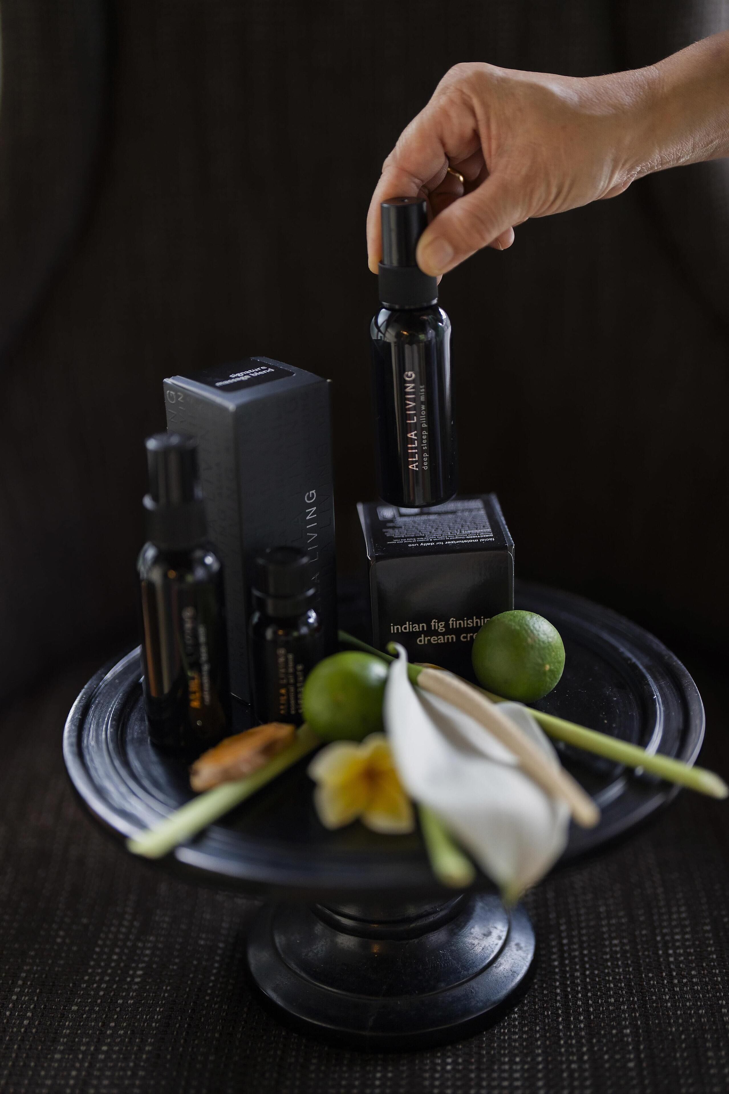 A hand holding a black spray bottle, surrounded by various black boxes and bottles on a black tray.