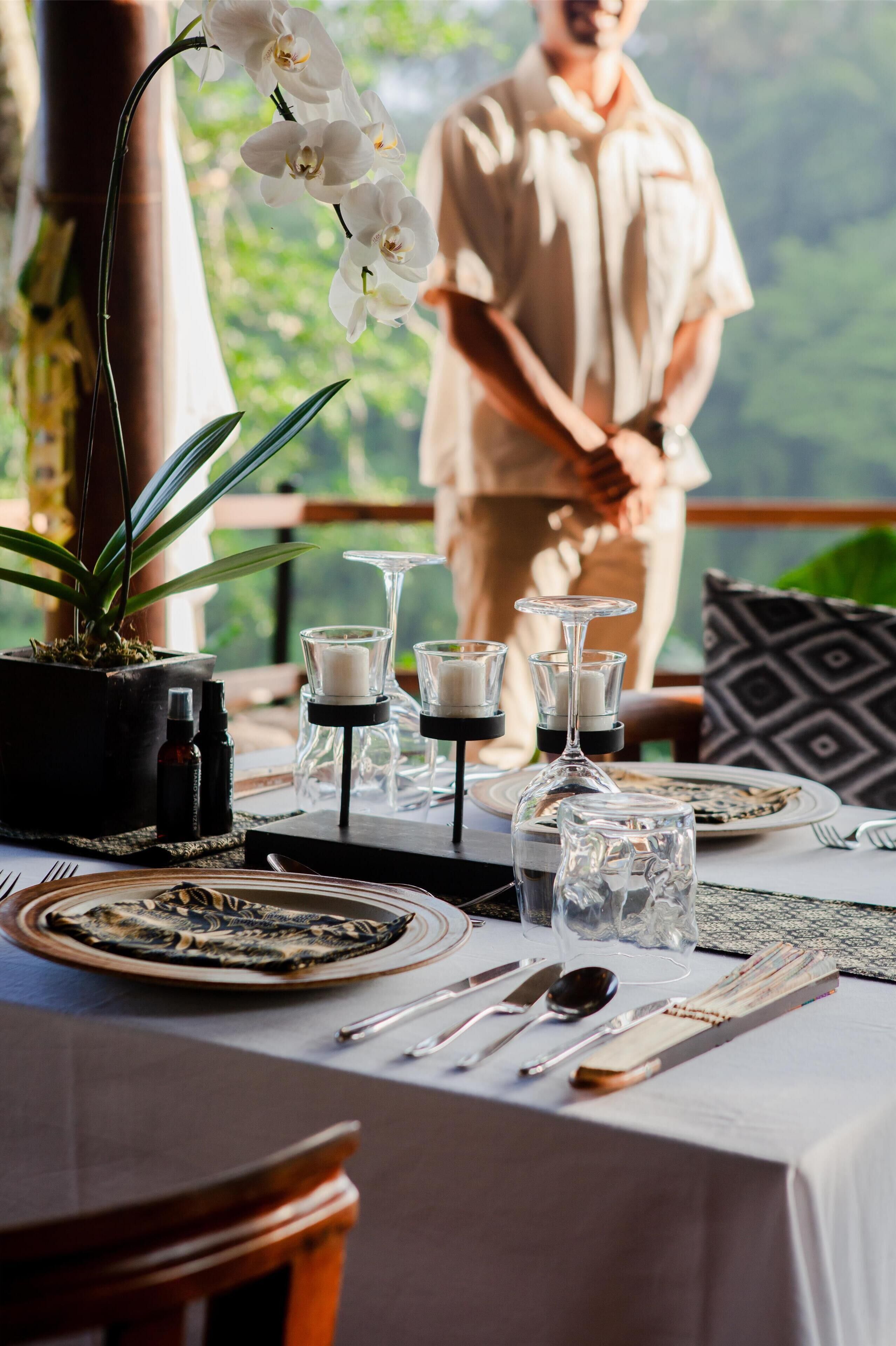 A table set with plates, cutlery, and candles, with a potted orchid and a bottle of oil on the table.