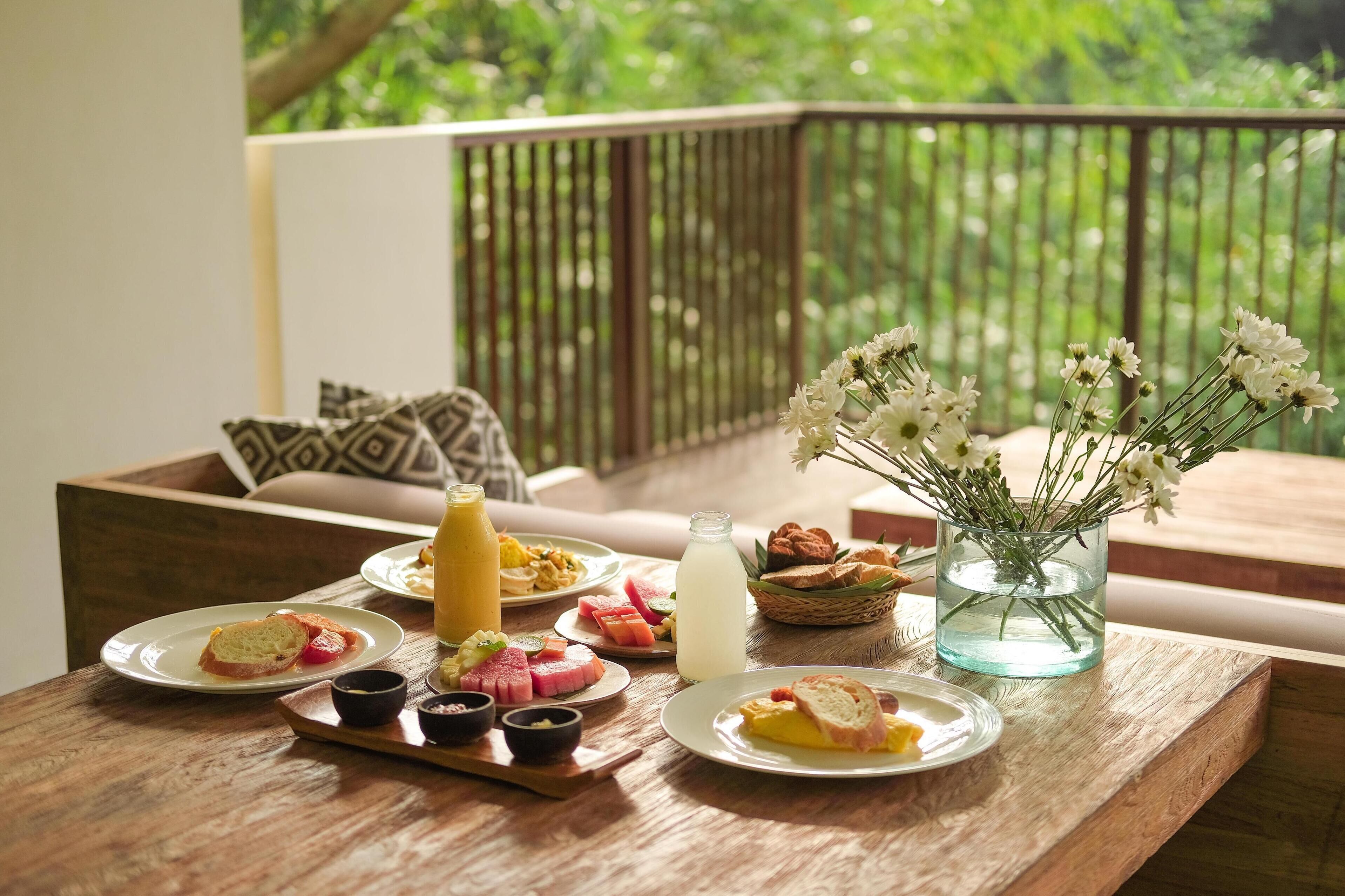 A breakfast setup on a wooden table with plates of food, a glass of juice, and a vase of flowers.