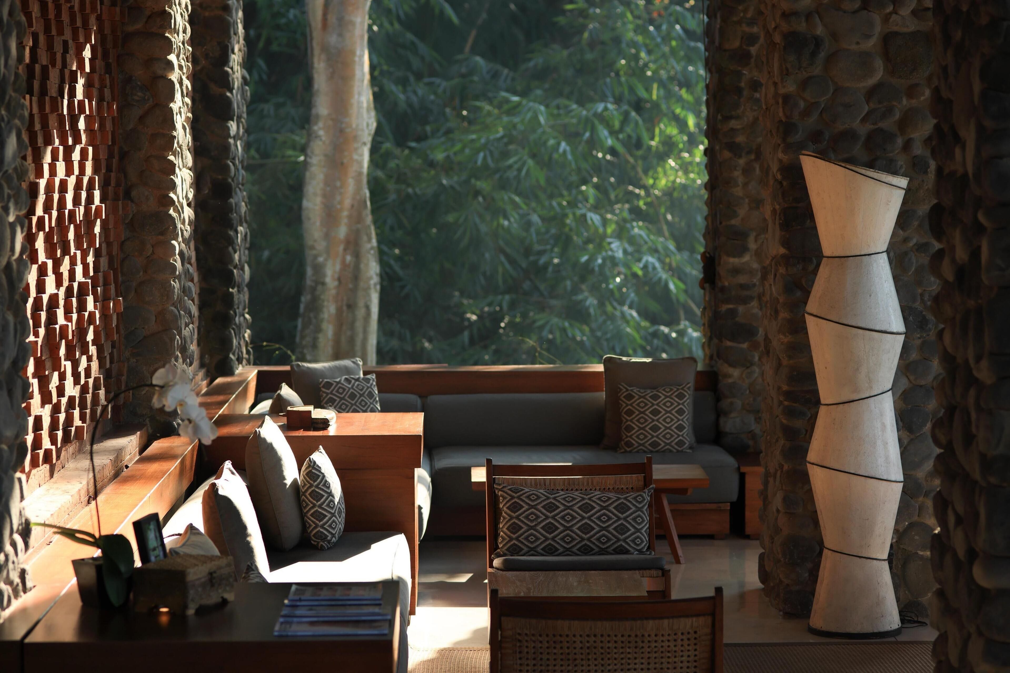 A cozy, well-lit room with a stone wall, a large vase, and a sofa with patterned cushions.