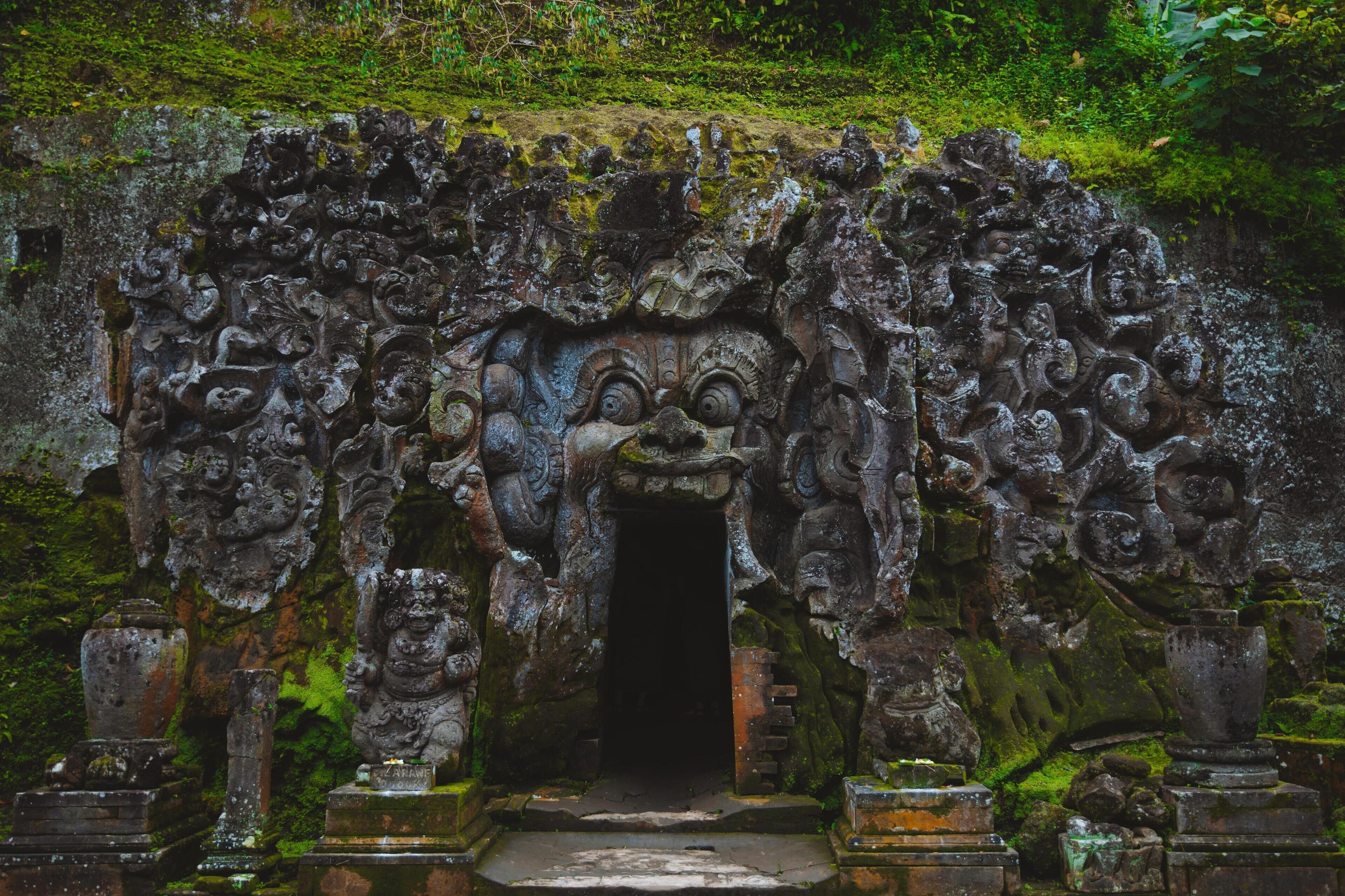 An ancient stone gateway with intricate carvings and a central doorway, surrounded by moss and vegetation.