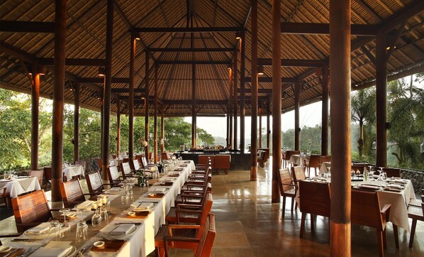 A long dining table set with chairs, a bar area, and a view of greenery outside.