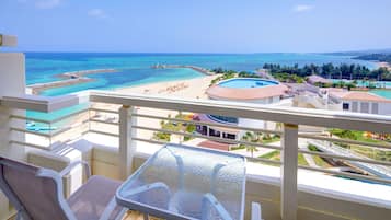 A balcony with a view of a beach, a pool, and a clear sky.