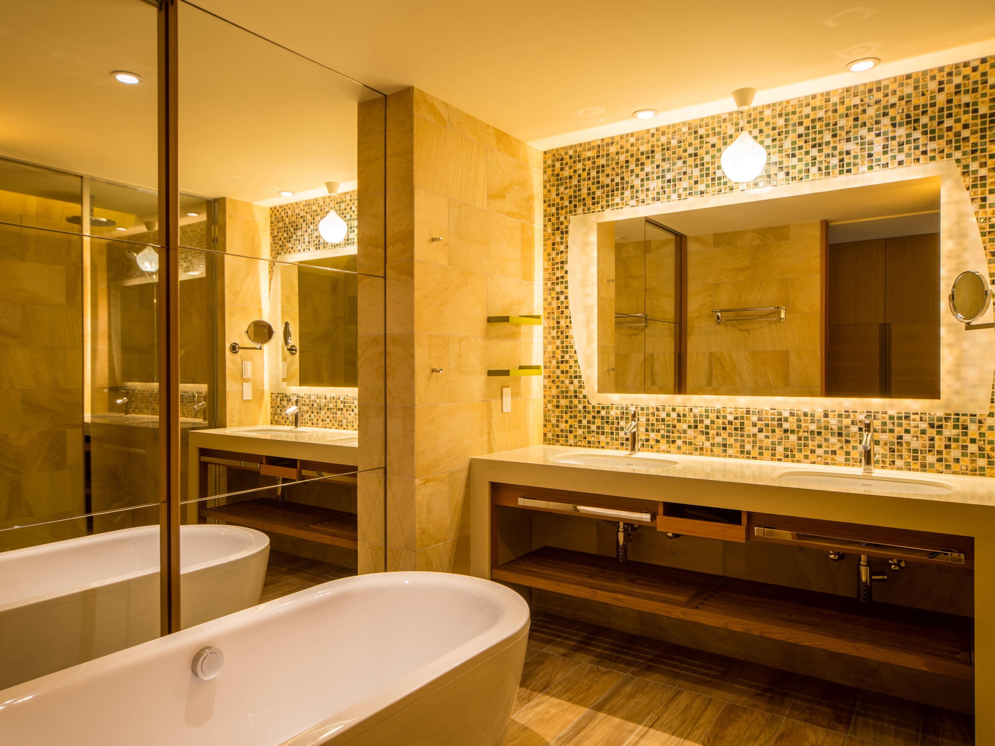 A modern bathroom with a large freestanding bathtub, two sinks, and a large mirror with mosaic tile backsplash.